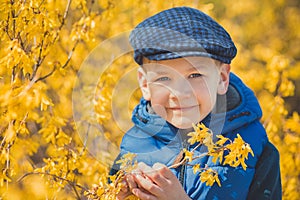 Cute handsome boy in stylish blue dress and hat close to yellow flowers enjoying spring time