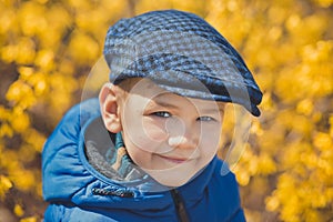 Cute handsome boy in stylish blue dress and hat close to yellow flowers enjoying spring time