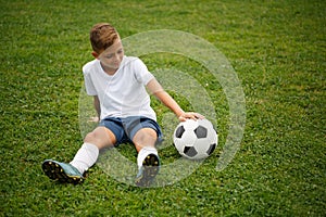 A cute, handsome guy with a soccer ball sitting on a green grass background. A football player at the stadium.