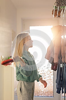 Cute happy 10 year little school girl child comb long blond hair with hairbrush near mirror against bright sun light in