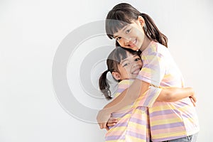 Cute happy Asian siblings hugging cuddling feeling love and connection, smiling kid girl sister embracing little girl sister on