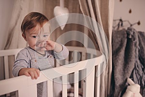 Cute happy baby boy awake in his bed in the morning and playing. Candid capture in real life interior