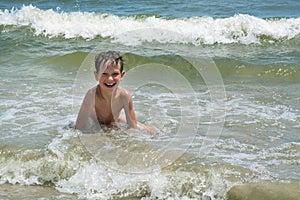 Cute happy baby boy bathes in the sea with waves, vacations.