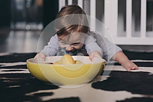 Cute happy baby boy eating cookies at home and playing with plate of lemons. Lifestyle indoor capture