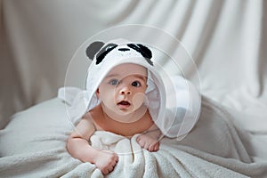 Cute happy baby boy in soft bathrobe after bath playing on white bed. Child in clean and dry towel. Wash, infant hygiene