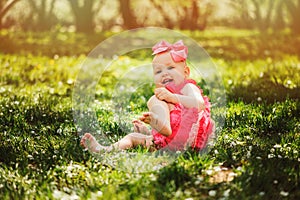 Cute happy baby girl in funny pink romper walking outdoor in spring garden