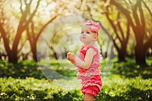 Cute happy baby girl in funny pink romper walking outdoor in spring garden