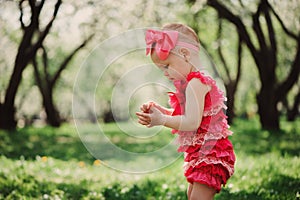 Cute happy baby girl in funny pink romper walking outdoor in spring garden