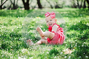 Cute happy baby girl in funny pink romper walking outdoor in spring garden