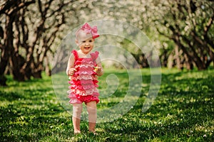 Cute happy baby girl in funny pink romper walking outdoor in spring garden photo