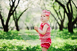 Cute happy baby girl in funny pink romper walking outdoor in spring garden photo
