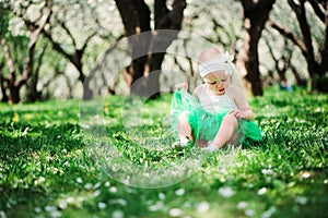 Cute happy baby girl in green tutu skirt walking outdoor in spring garden