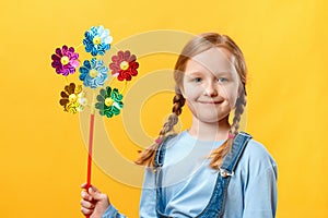 Cute happy beautiful little girl holding a pinwheel toy. Child close-up on a yellow background