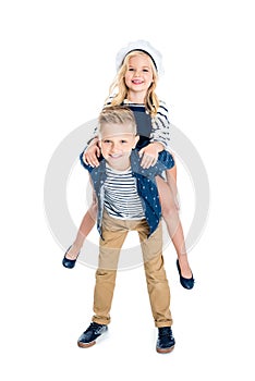 cute happy boy piggybacking adorable little sister smiling at camera