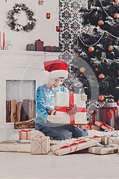 Cute happy boy in santa hat unwrapping christmas presents