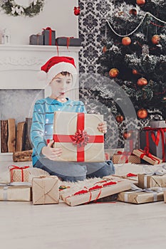 Cute happy boy in santa hat unwrapping christmas presents