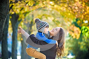 Cute, happy, boy smiling and hugging with his mom among yellow leaves. Little child having fun with mother in autumn park. Concept