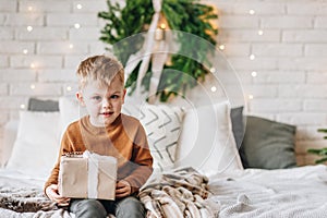 Cute happy Caucasian boy opening his presents on Christmas morning. Christmas tree wreath on background. Child excited