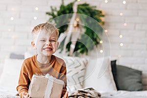 Cute happy Caucasian boy opening his presents on Christmas morning. Christmas tree wreath on background. Child excited