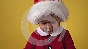 Cute Happy Cheerful Chubby Toddler Baby Girl in Santa Suit Looking On Camera At Yellow Background. Child Playing