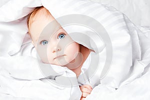 Cute and Happy child with blue eyes looking out of the white blanket. Copy space.