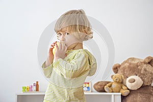 Cute happy child boy having fun eating a big fresh yellow apple fruit at home. Children healthy eating and lifestyle conceptual