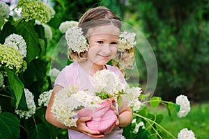 Cute happy child girl with hydrangea flowers bouquet in summer garden