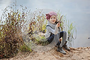Cute happy child girl playing on the river side in autumn