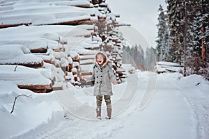 Cute happy child girl portrait on the walk in winter forest with tree felling on background