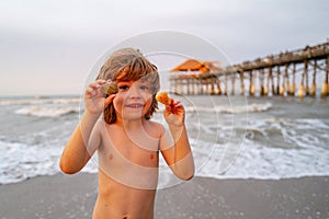 Cute, happy child holding shell at the beach. Cute little boy at tropical beach holding sand shell. Summer travel and