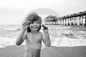 Cute, happy child holding shell at the beach. Cute little boy at tropical beach holding sand shell. Summer travel and