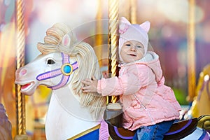 Cute happy child riding the horse on the colorful merry go round