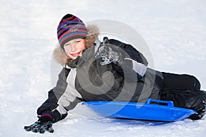 Cute happy child wearing warm clothes sledding and showing thumbs up