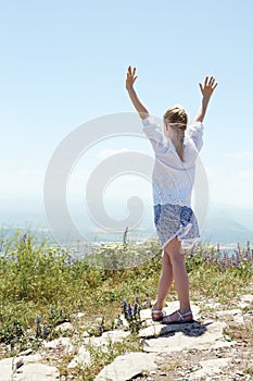 Cute happy child in white blouse on a rock with raised hands