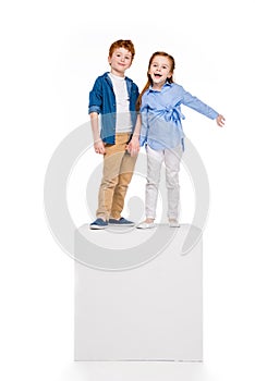 cute happy children standing on white cube and smiling at camera