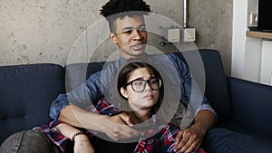 Cute happy couple of young hipsters lying on the couch, trying to find a perfect tv channel. Leisure time, enjoying