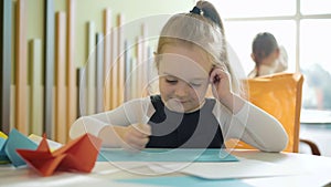 Cute happy girl drawing picture with classmates sitting at the background. Portrait of positive pretty Caucasian