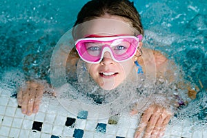 Cute happy girl in pink goggles mask in the swimming pool