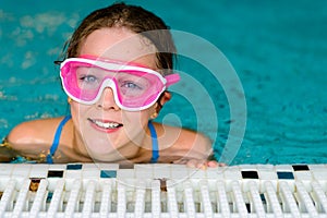 Cute happy girl in pink goggles mask in the swimming pool