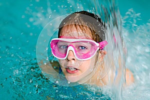 Cute happy girl in pink goggles mask in the swimming pool