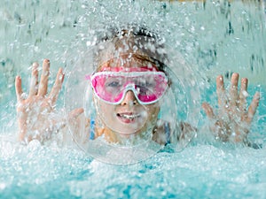 Cute happy girl in pink goggles mask in the swimming pool