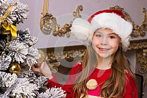 Cute happy girl in red hat hangs decorations