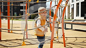 Cute happy laughing baby boy having fun on the playground with ropes and nets. Children playing outdoor, kids outside, summer