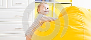 Cute happy laughing baby boy playing on white bedroom.