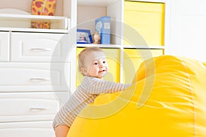 Cute happy laughing baby boy playing on white bedroom.