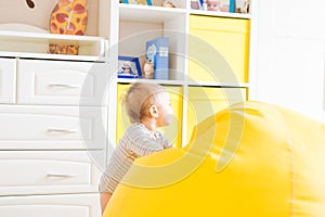 Cute happy laughing baby boy playing on white bedroom.