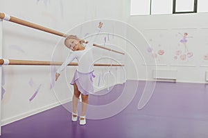 Cute happy little ballerina exercising at dancing school