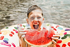 Happy little boy having fun in rubber ring eating juicy watermelon