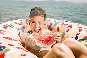 Happy little boy having fun in rubber ring eating juicy watermelon