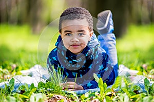 Cute happy little boy lying in green grass on spring